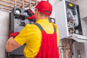 HVAC technician in yellow and red uniform performing furnace repair in a residential property