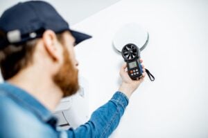 Indoor air quality specialist checking HVAC airflow with an anemometer during air testing.