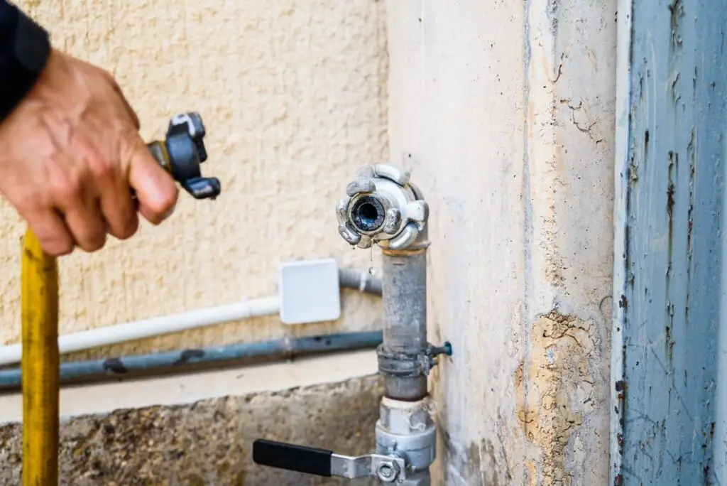 Technician connecting a yellow hose to a water valve during an urgent plumbing repair